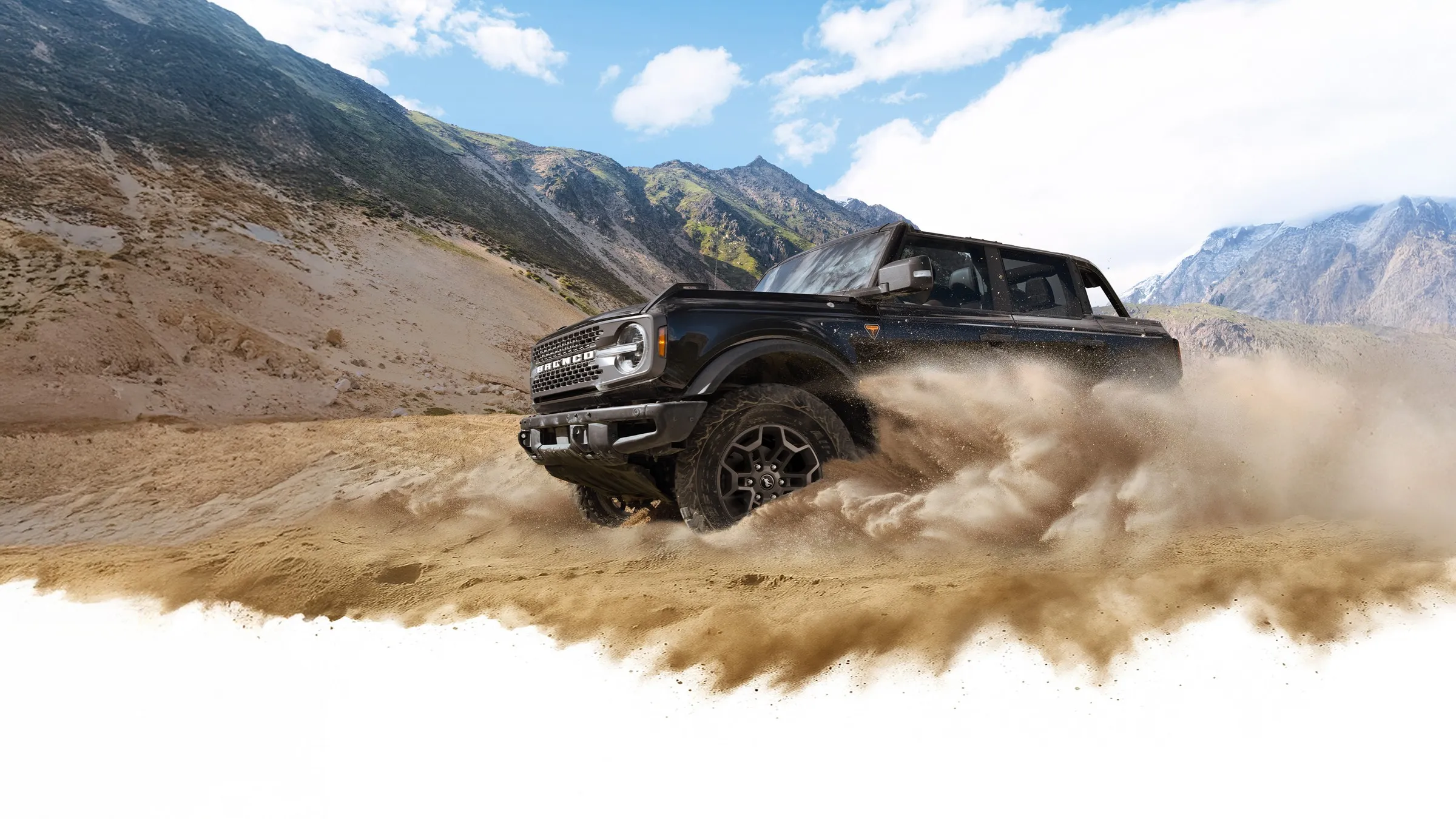 A Ford Bronco® kicking up dust in a valley beneath rocky hills