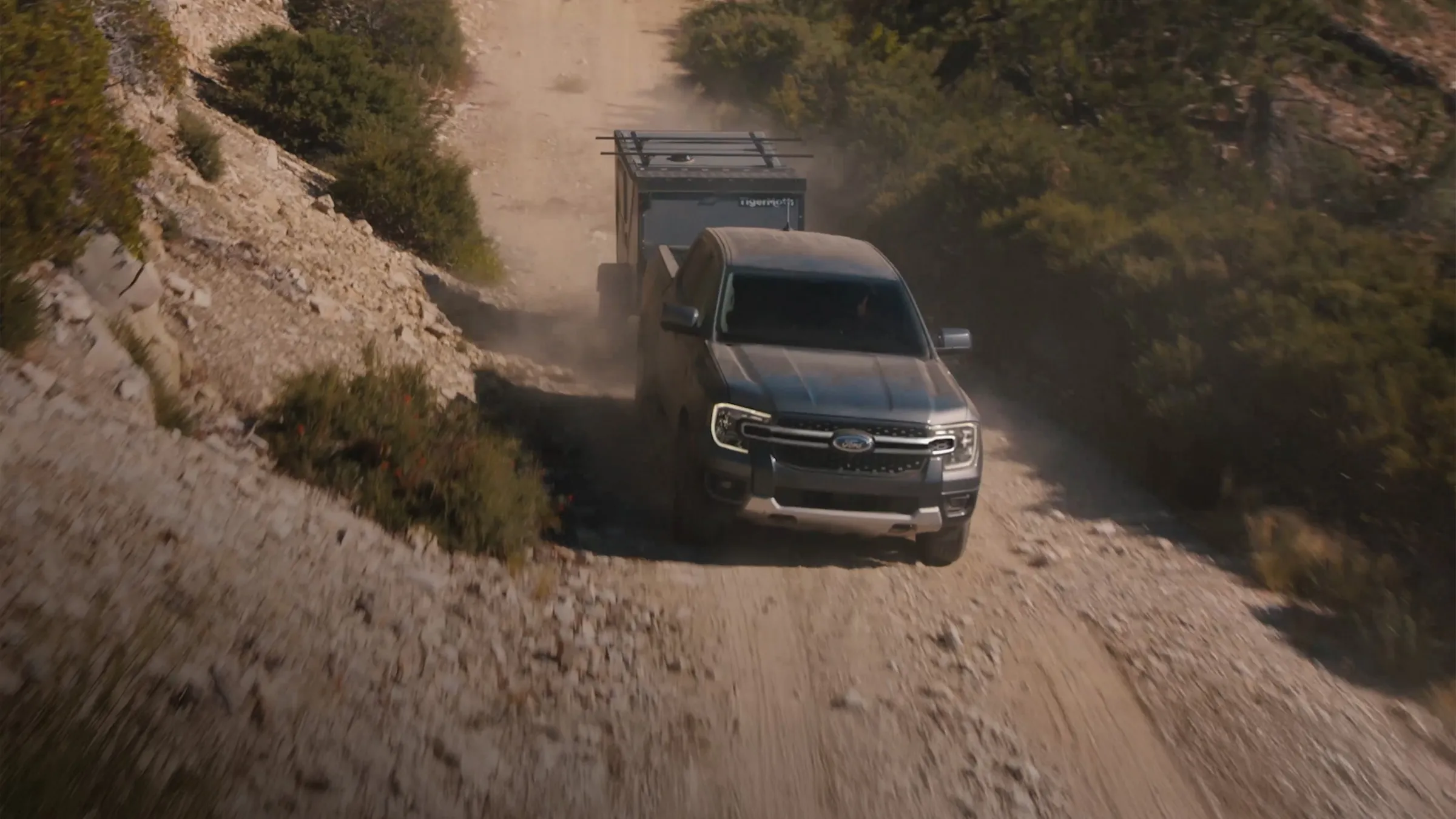 A Ford Ranger® towing a trailer on a dirt road in the mountains